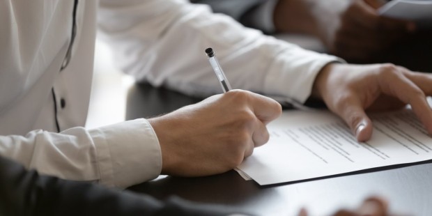 A person signs a form at a desk.