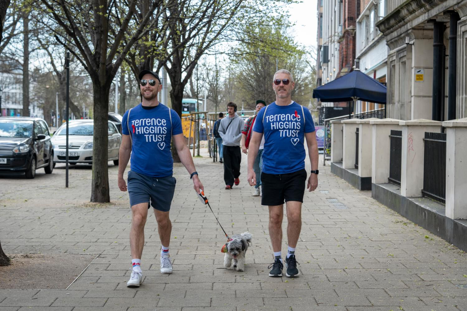 Two men in Terrence Higgins Trust t-shirts with a dog on a leash. Two men in Terrence Higgins Trust t-shirts with a dog on a leash.