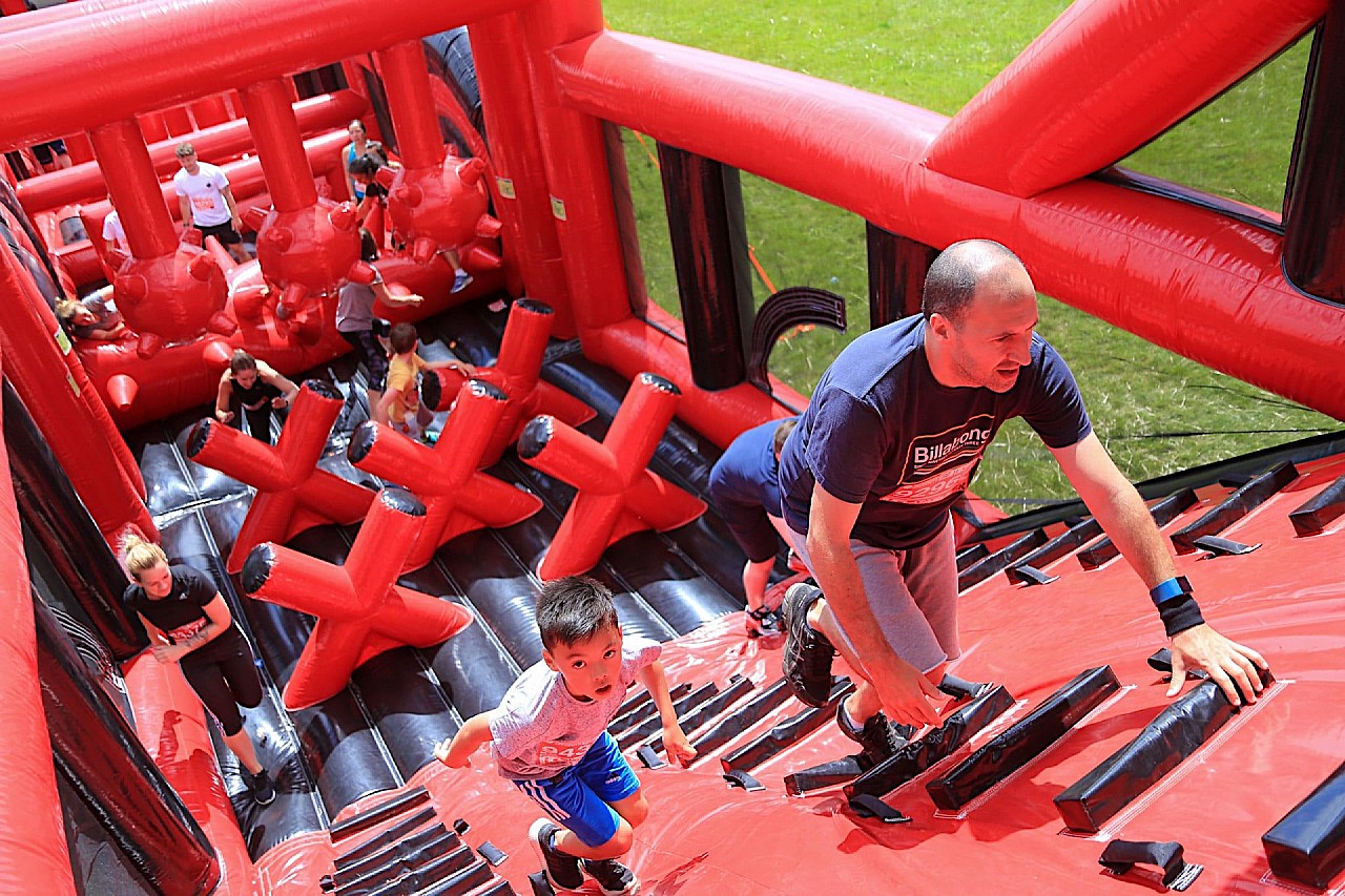 Obstacle course racers climbing a bouncy red diagonal wall