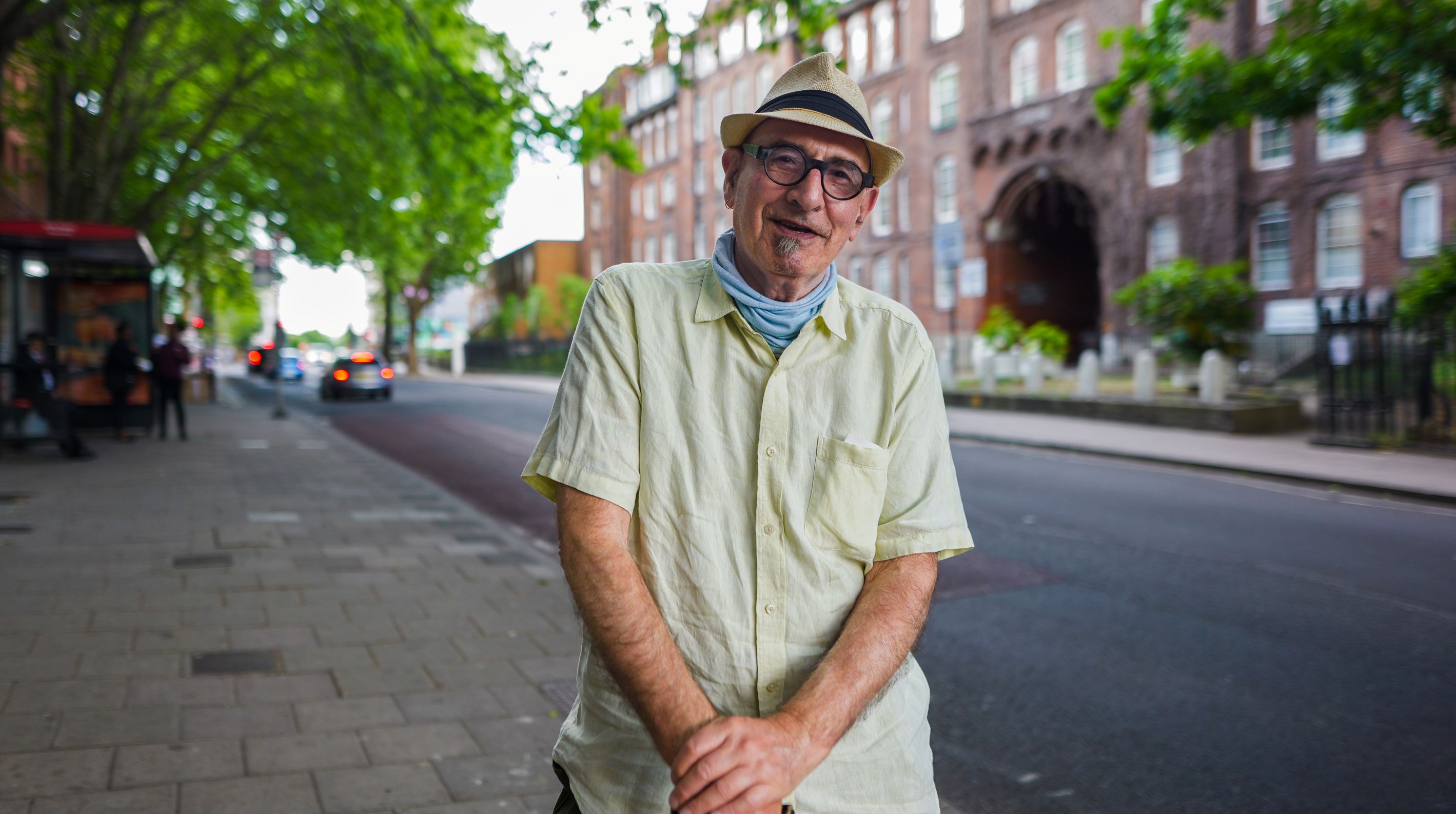 An elderly bespectacled with a hat smiling.