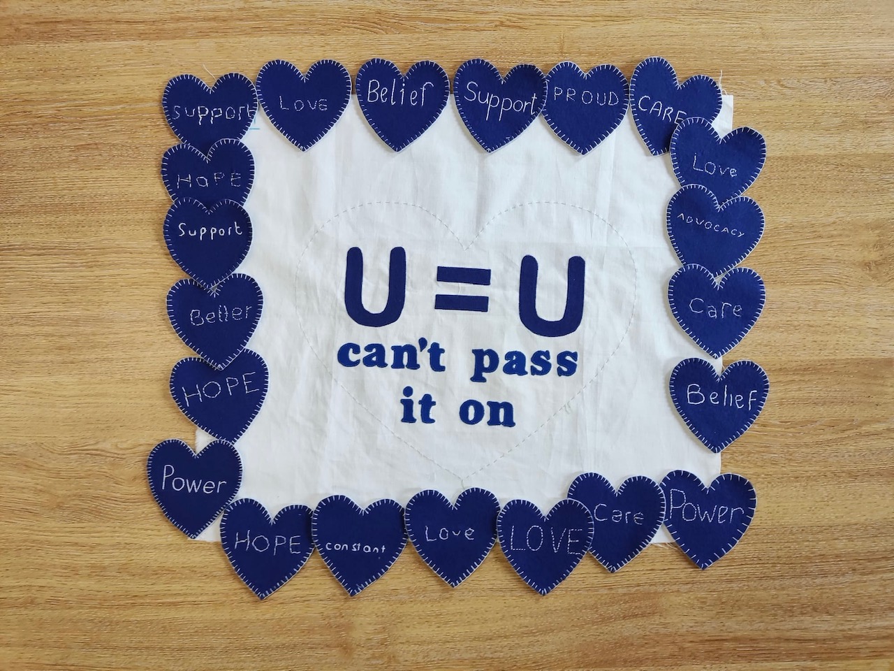 Terry Higgins Memorial Quilt panel piece reading "U=U can't pass it on" surrounded in blue hearts, photo credited to credit @handmadebygeraldine and @sarahashfordstudio 