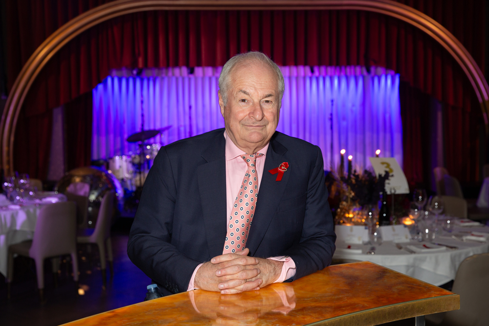 Paul Gambacini with red ribbon sat at desk at An Evening Of Radio Magic venue