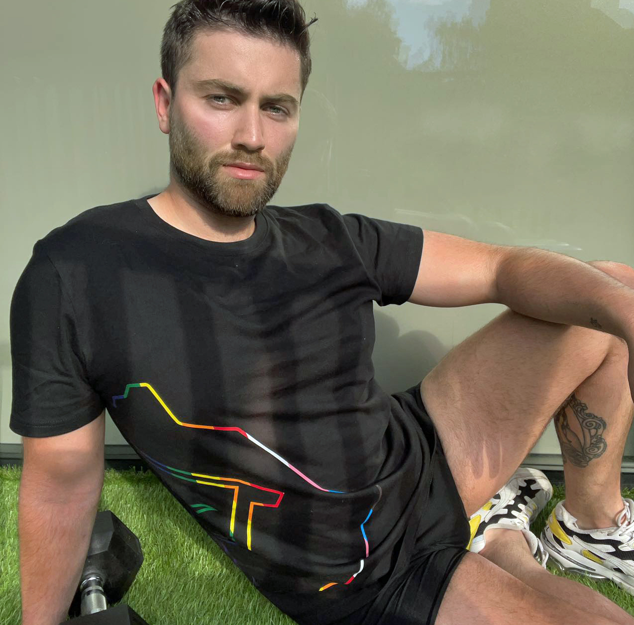 Den's pride t-shirt, showing black with rainbow logo, as worn by a model
