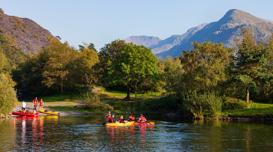 People in kayaks on a lake with mountainous Welsh landscape behind them
