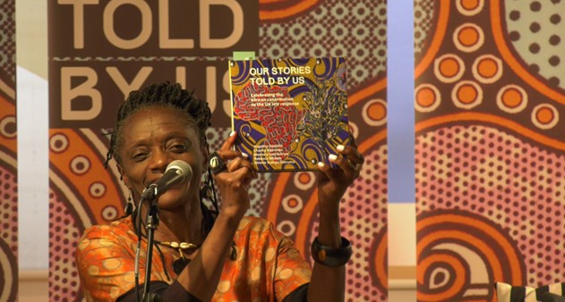 Winnie Ssanyu Sseruma holding up a copy of Our Stories Told By Us book