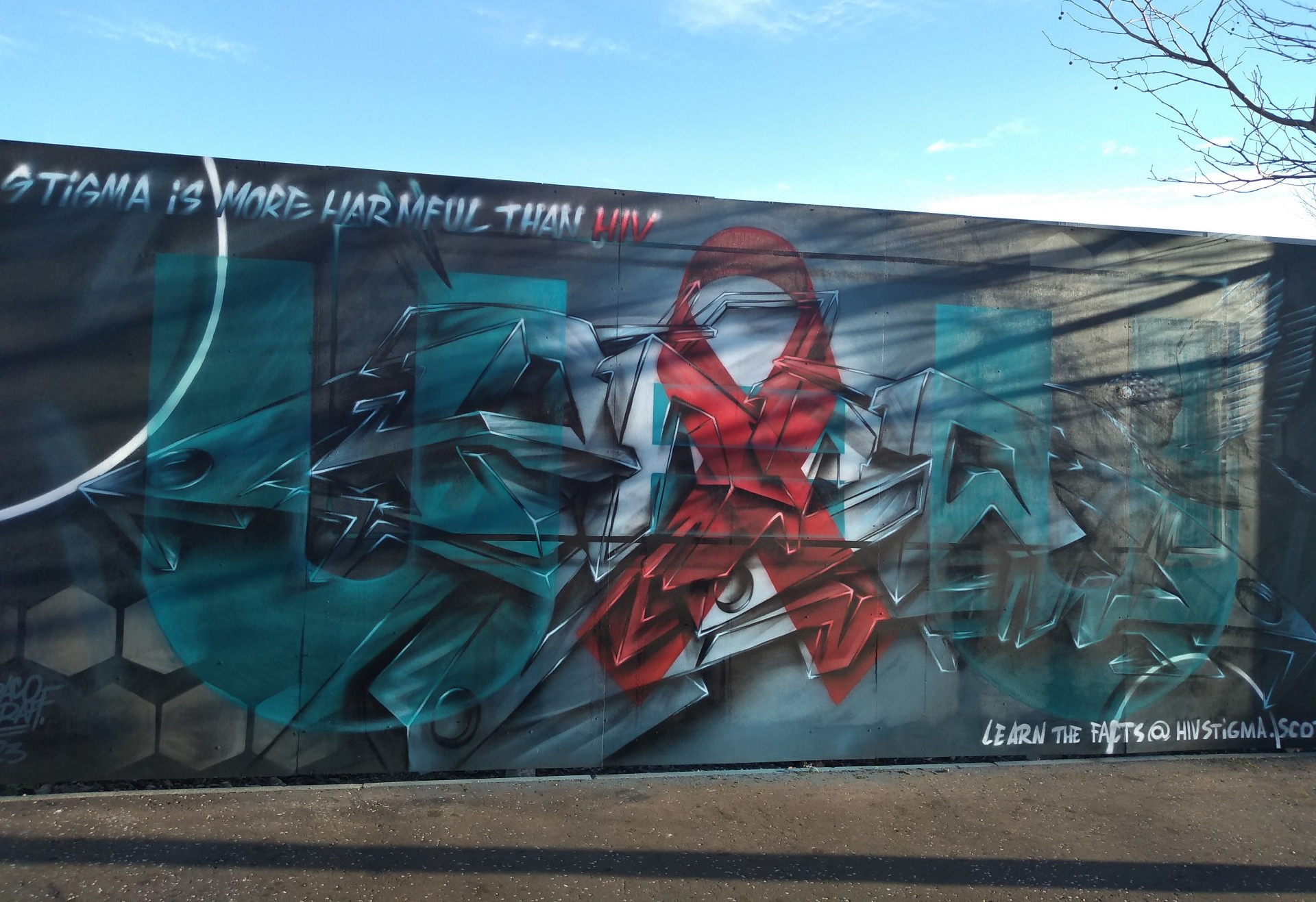 Wall mural in Dundee with red ribbon and message reading "stigma is more harmful than HIV"