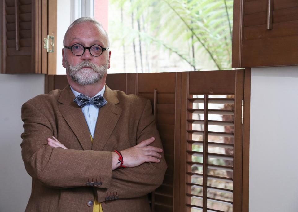 An elderly bespectacled and bearded man with his arms crossed.
