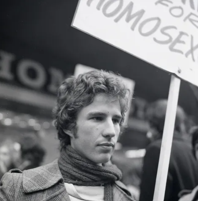 Image of Tony Whitehead at a protest holding a sign and wearing a scarf and jacket