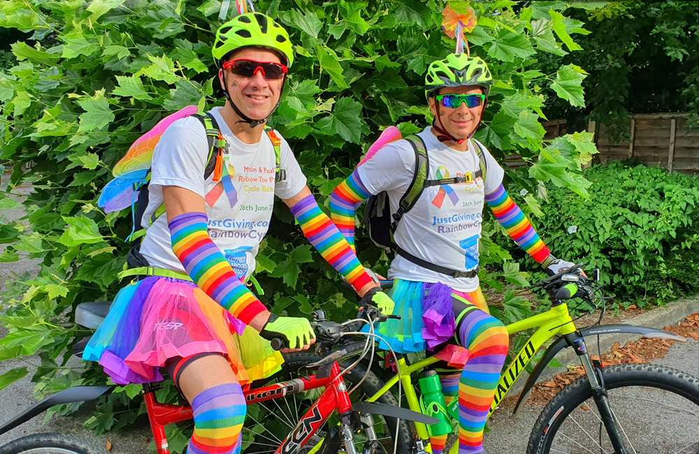 Two smiling cyclists in rainbow attire.