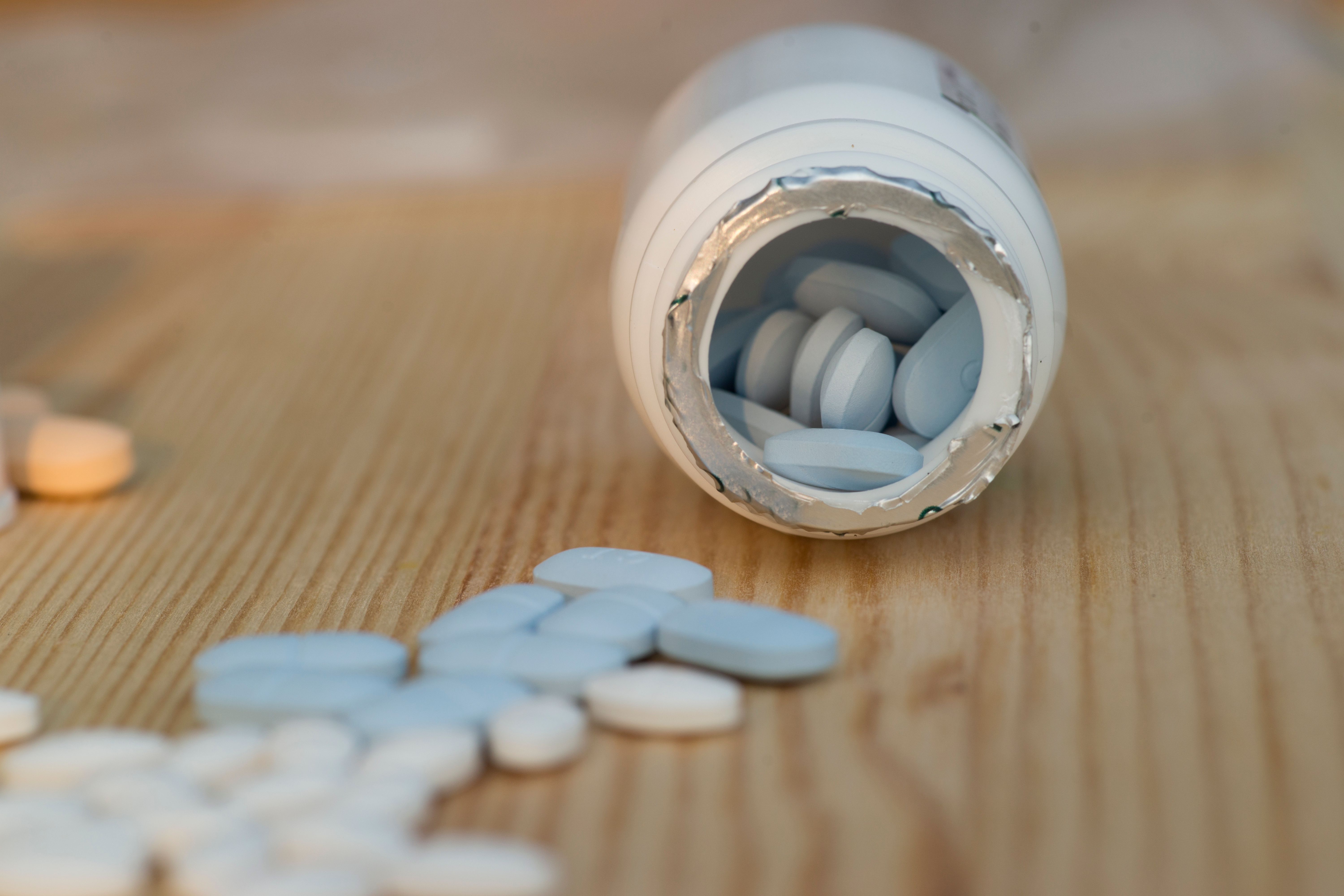 A white bottle on a wooden background with blue and white pills.