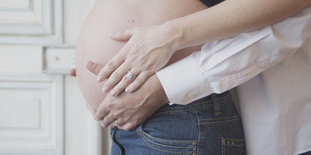 Pregnant woman with partner's hands on stomach