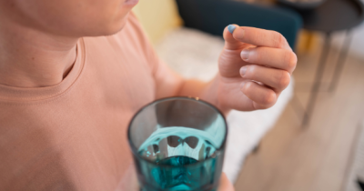 PrEP block Person holding a blue pill in their hand and a glass of water.