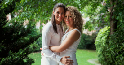 Two newly married women hugging in white outfits