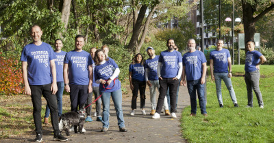 Large group of Ribbon Walk people in THT shirts in park with dog Large group of Ribbon Walk people in THT shirts in park with dog
