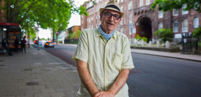 An elderly bespectacled with a hat smiling.