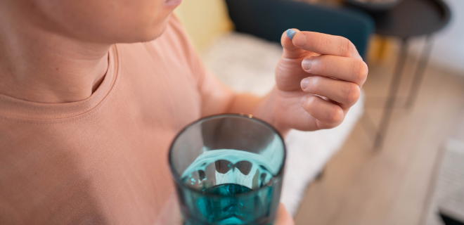 Person holding a blue pill in their hand and a glass of water.