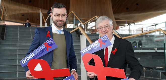 Rhys Goode and Mark Drakeford with posters saying "we can end new cases of HIV by 2030 but we need action now" in English and Welsh