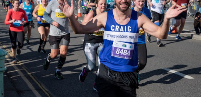 A smiling and waving Terrence Higgins Trust marathon runner.
