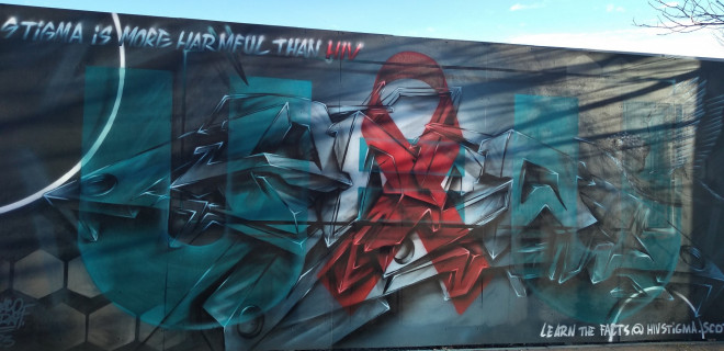 Wall mural in Dundee with red ribbon and message reading "stigma is more harmful than HIV"