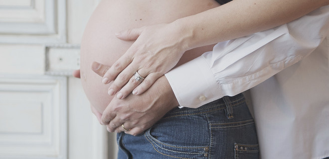 Pregnant woman with partner's hands on stomach