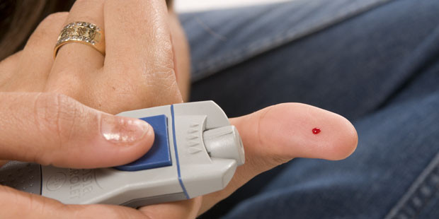 Someone holding a device to measure blood sugar for diabetes, with a blood of drop on the finger