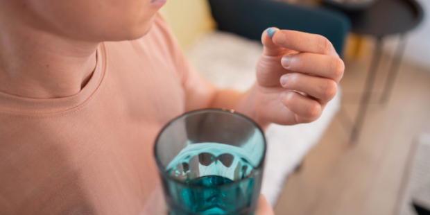 Person holding a blue pill in their hand and a glass of water.