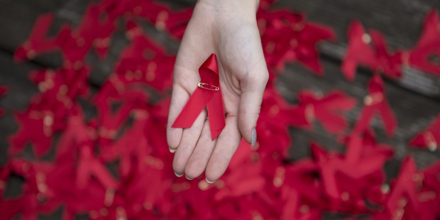 One hand holding one red ribbon One hand holding one red ribbon