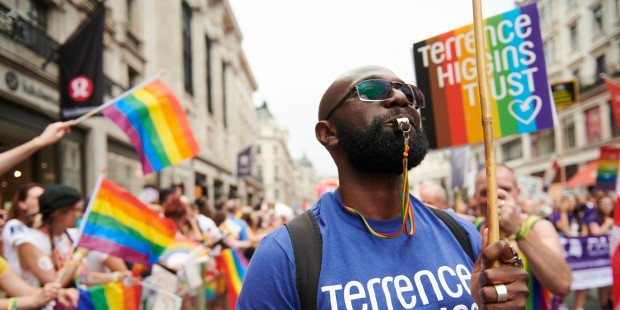Man in Terrence Higgins Trust T-shirt blowing whistle at Pride
